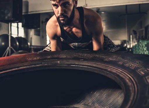 Man focusing intensely while flipping a large tire during a crossfit workout in a gym.